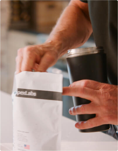 Person placing items into a white bag while holding a black cup.