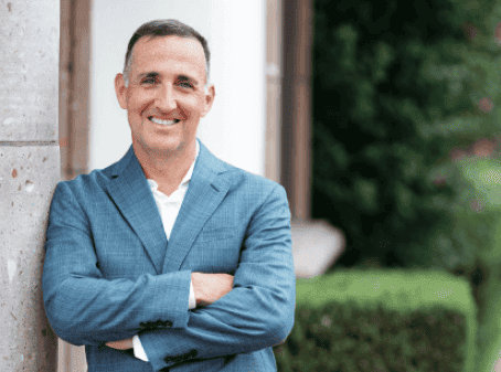 Man in a blue suit smiling with arms crossed, standing outdoors.