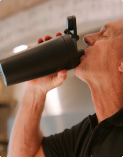 Person drinking from a black shaker bottle indoors.