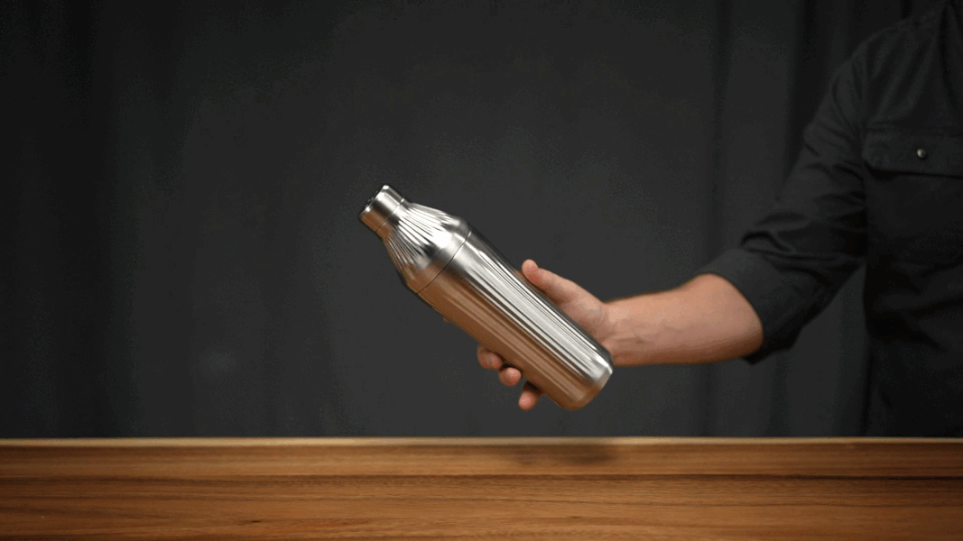 Person holding a stainless steel cocktail shaker over a wooden surface.
