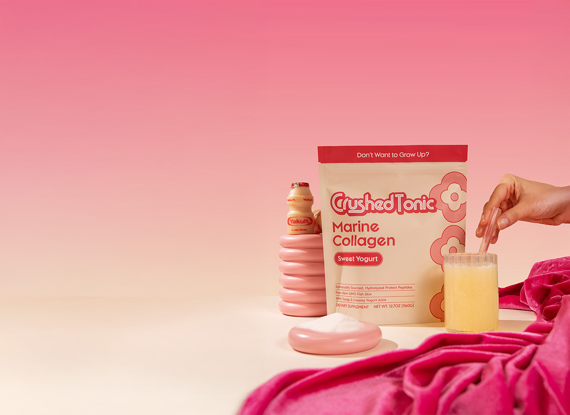 Package of Crushed Tonic Marine Collagen with a hand stirring a glass, pink background.