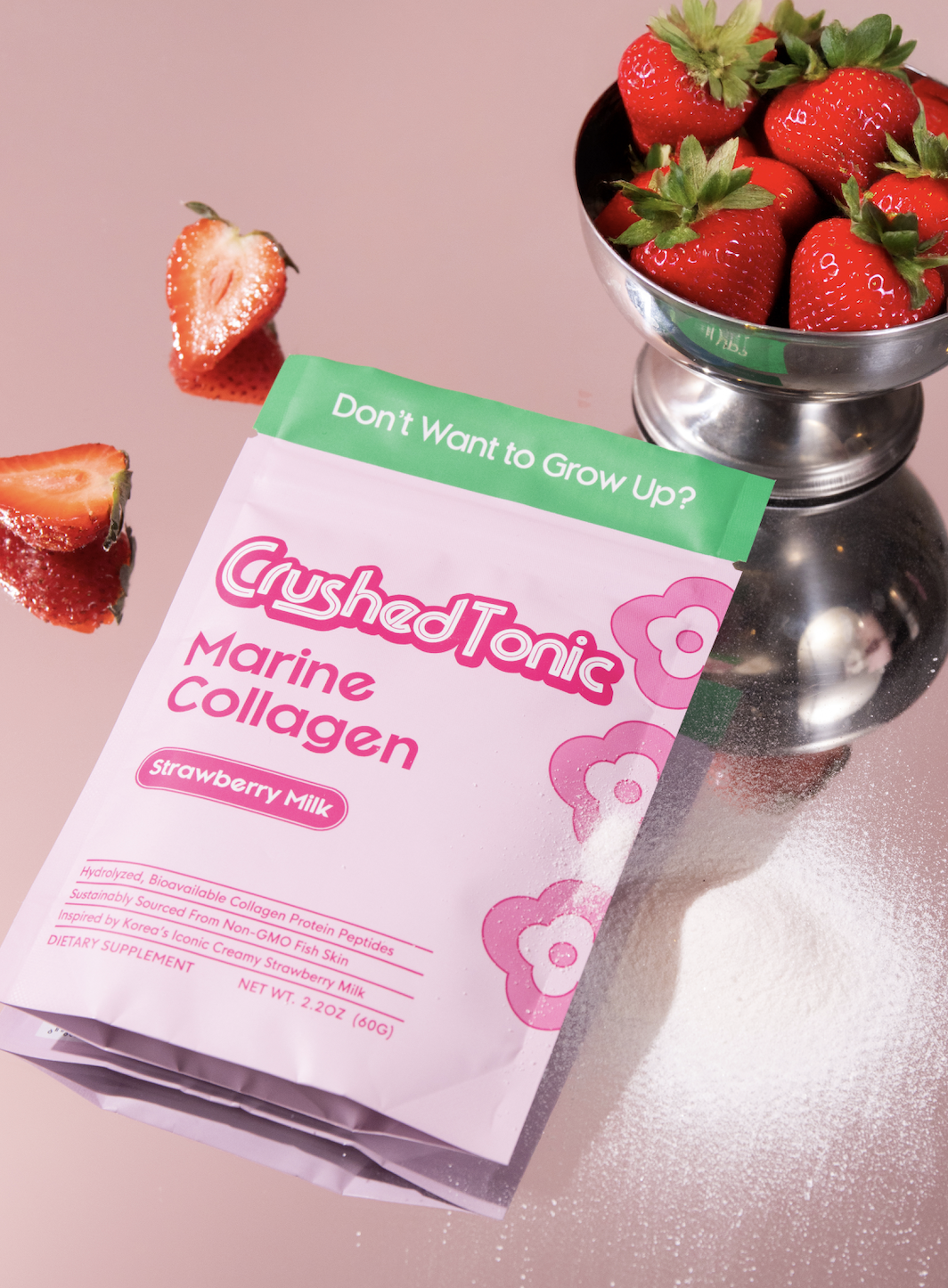 A pouch of Crushed Tonic Strawberry Milk collagen next to a bowl of fresh strawberries on a reflective surface.