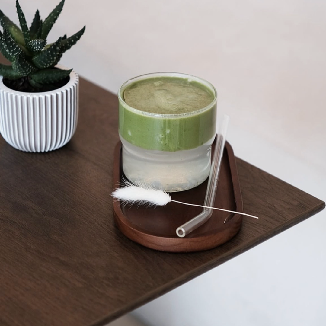 A glass of matcha latte on a wooden tray next to a potted succulent on a shelf.