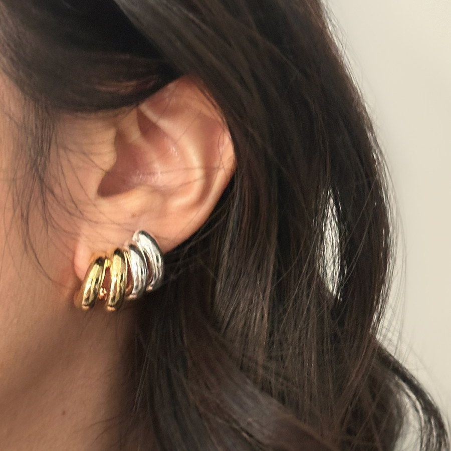 Close-up of a woman's ear with gold and silver hoop earrings.