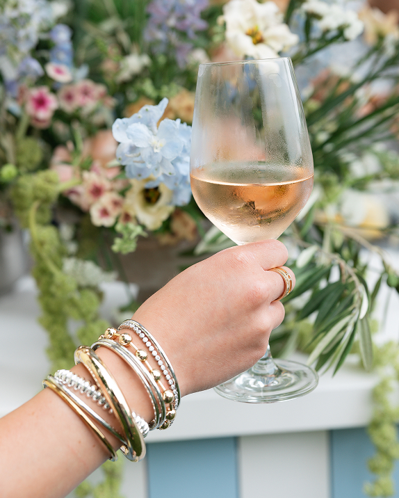 Hand holding a wine glass with flowers in the background.