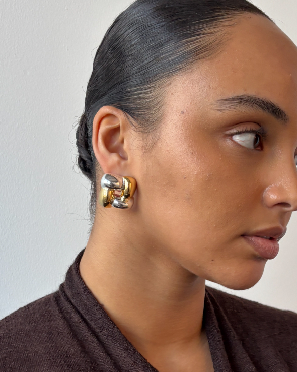 A close-up of a model wearing a large, two-toned, interwoven gold and silver earring.