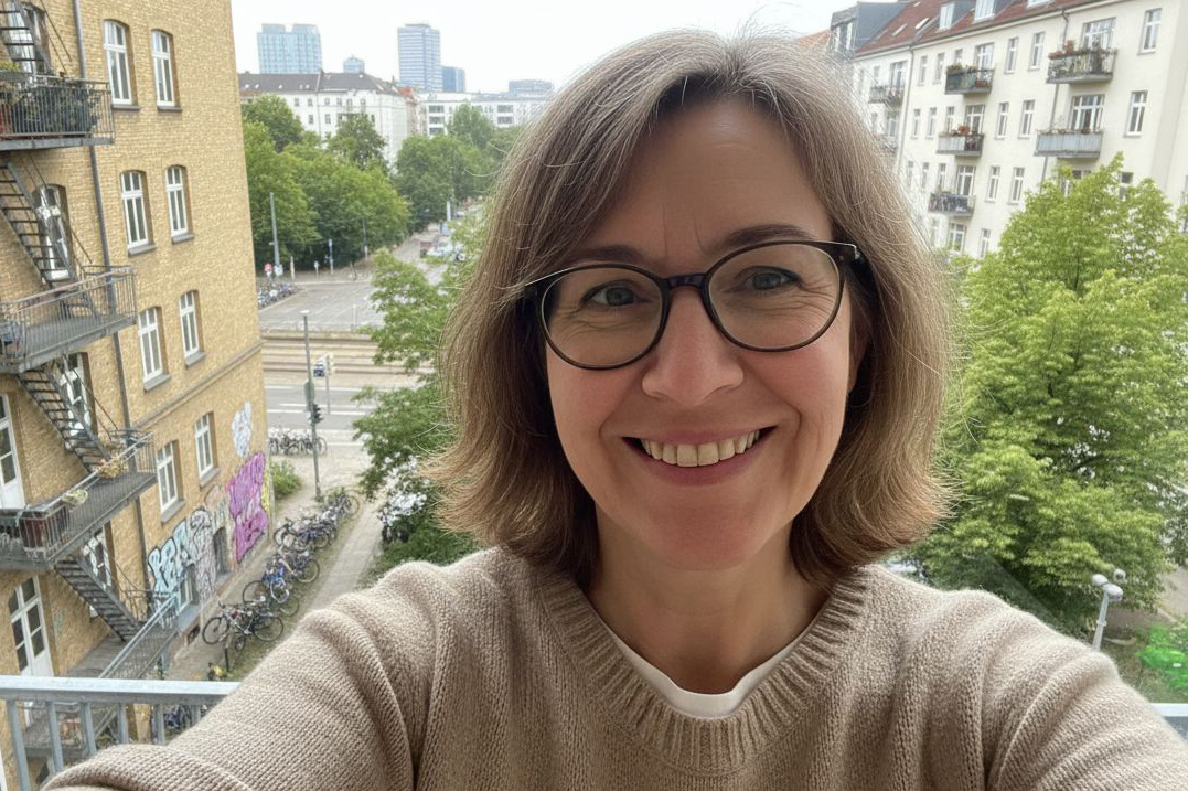 A person smiling on a balcony with a cityscape background.