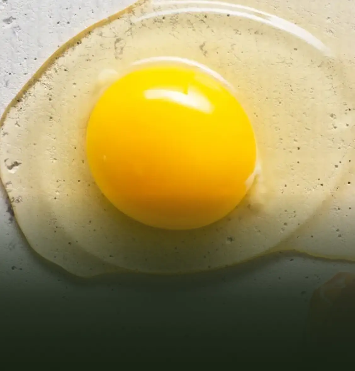 A raw egg with a bright yellow yolk on a flat surface.