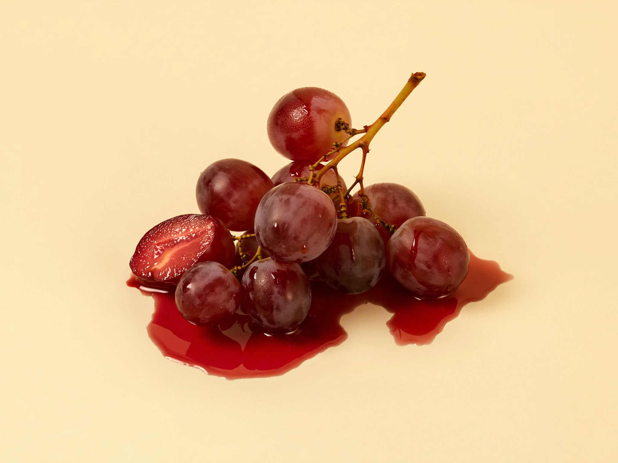 Cluster of red grapes and juice puddle on beige background.