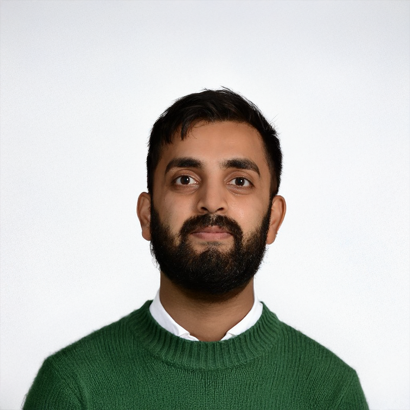 Person with a beard wearing a green sweater against a plain background.