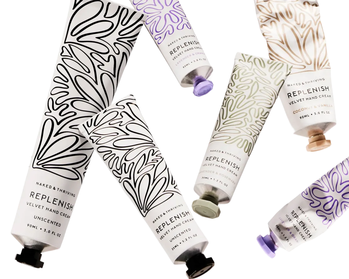Several tubes of Naked & Thriving's Replenish Velvet Hand Cream are scattered on a white background.