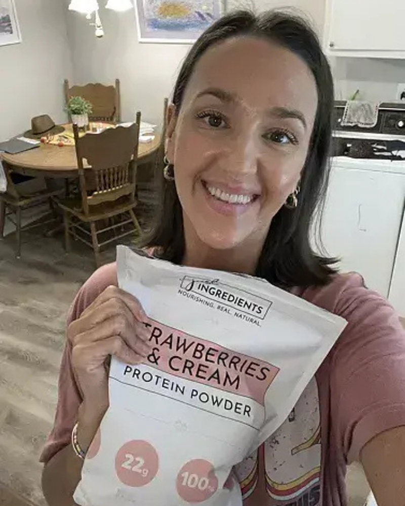 Woman holding a bag of strawberries and cream protein powder in a kitchen.