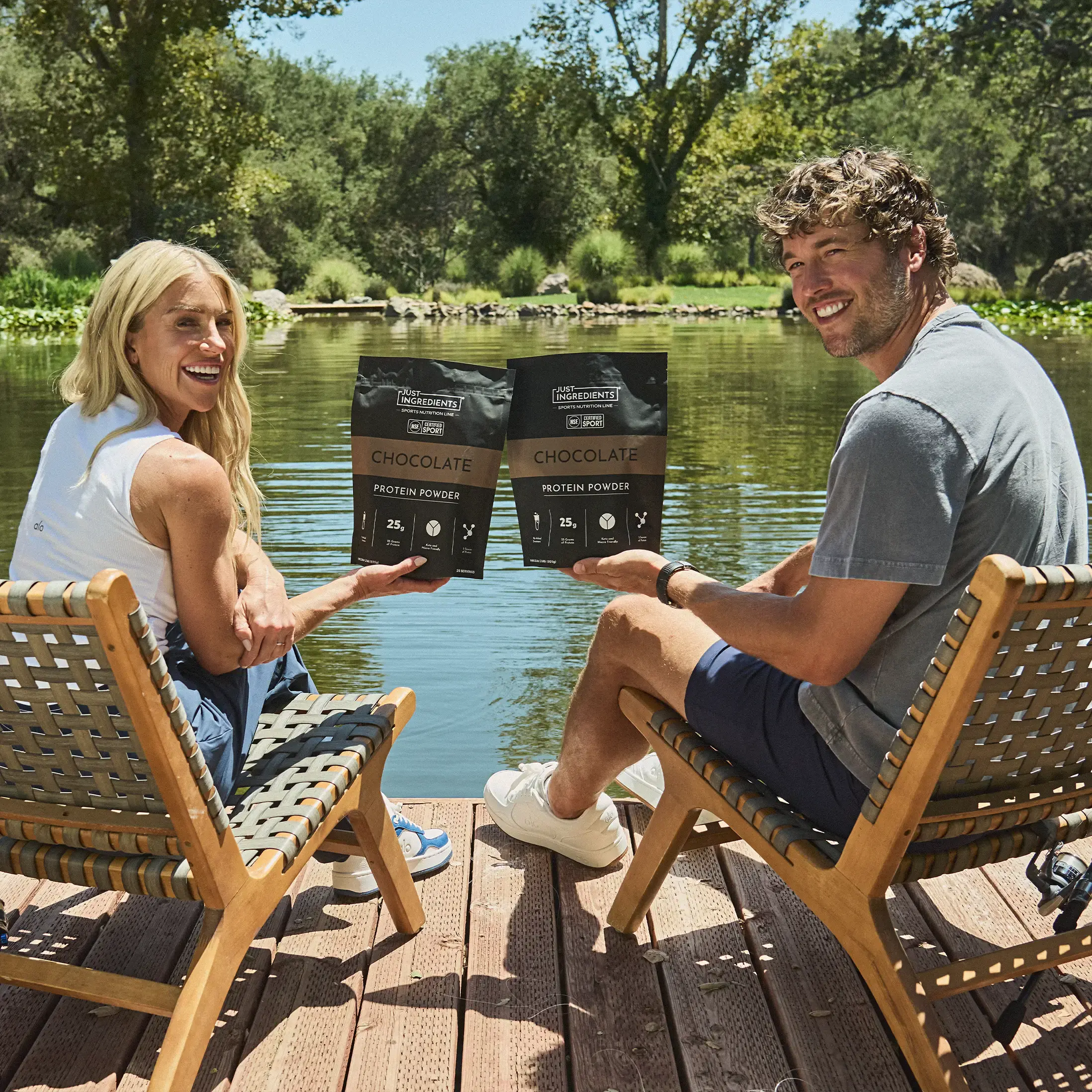 A man and a woman sit on chairs on a dock, holding bags of chocolate protein powder.