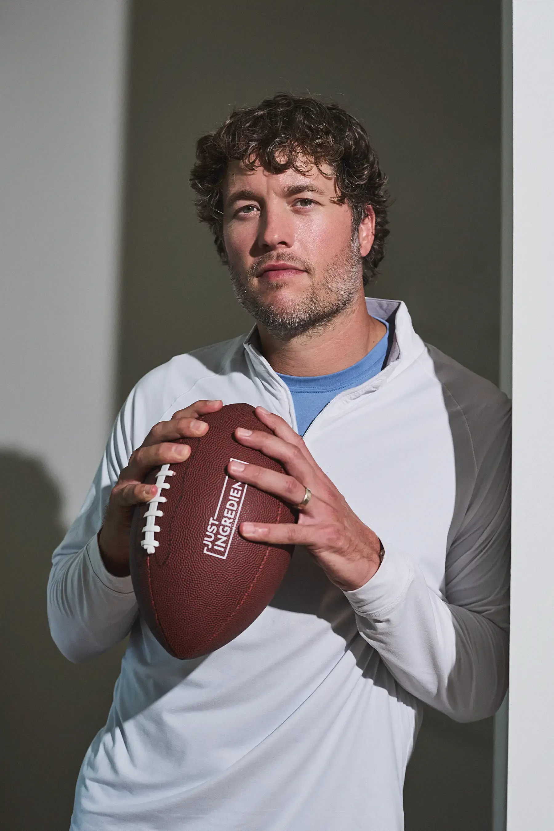 A man with curly hair holds a football with the 'Just Ingredients' logo on it.