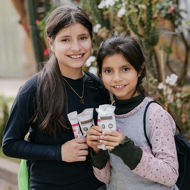 Two smiling girls holding chocolate bars outdoors.