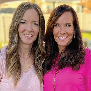 Two smiling women standing outdoors with a blurred background.