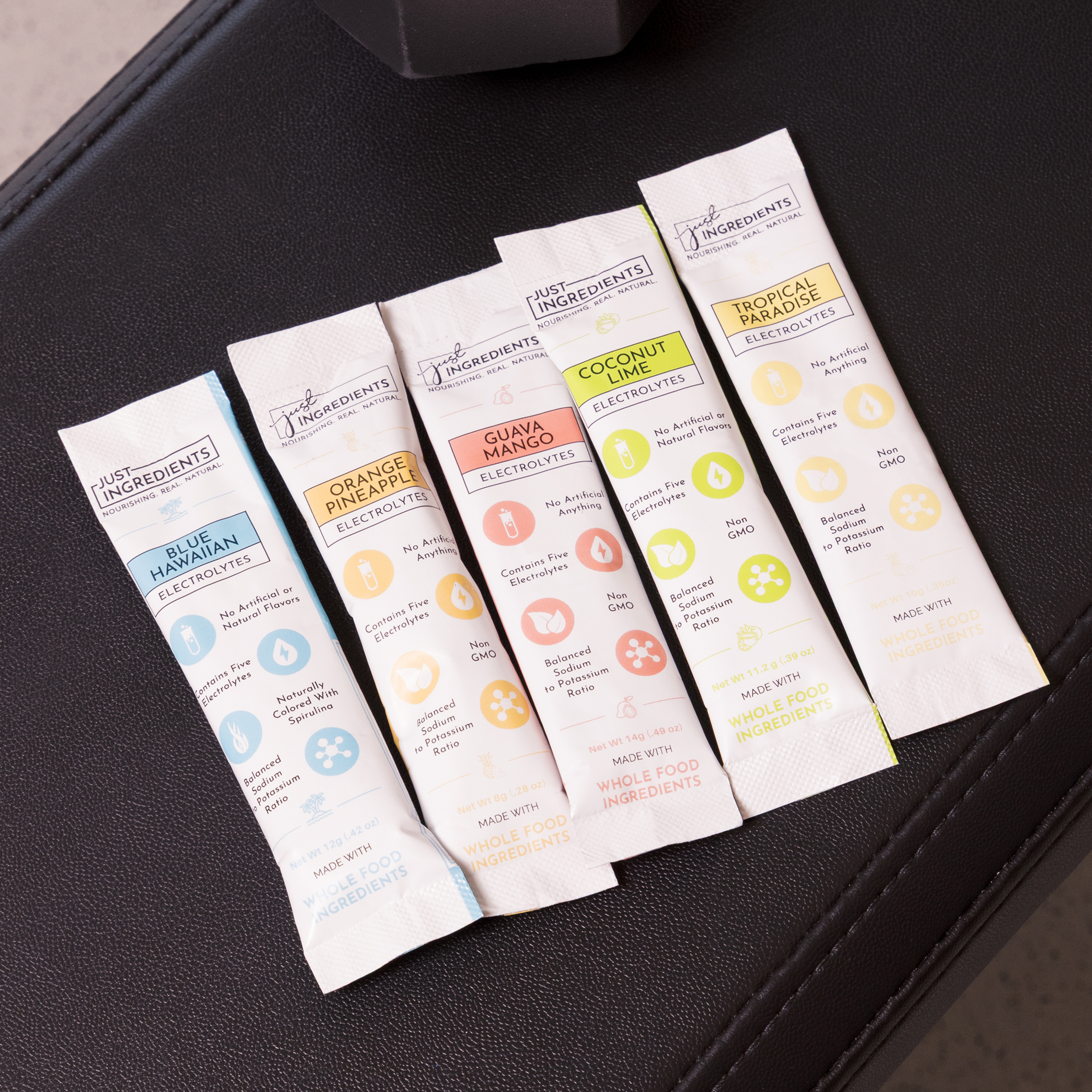 Five electrolyte drink mix packets in various flavors on a black surface.