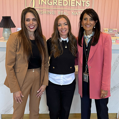 Three women smiling, standing together in a business setting.