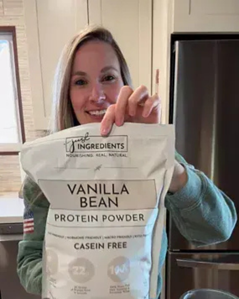 Person holding a bag of vanilla bean protein powder in a kitchen.