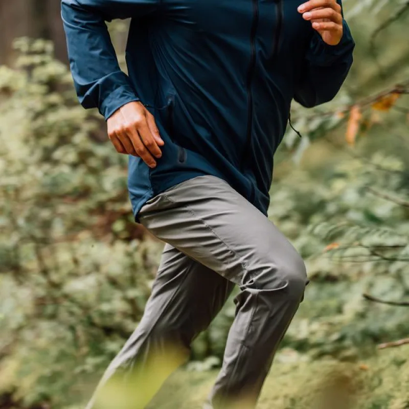 A person running outdoors wearing a blue jacket and grey pants, seen from the waist down.