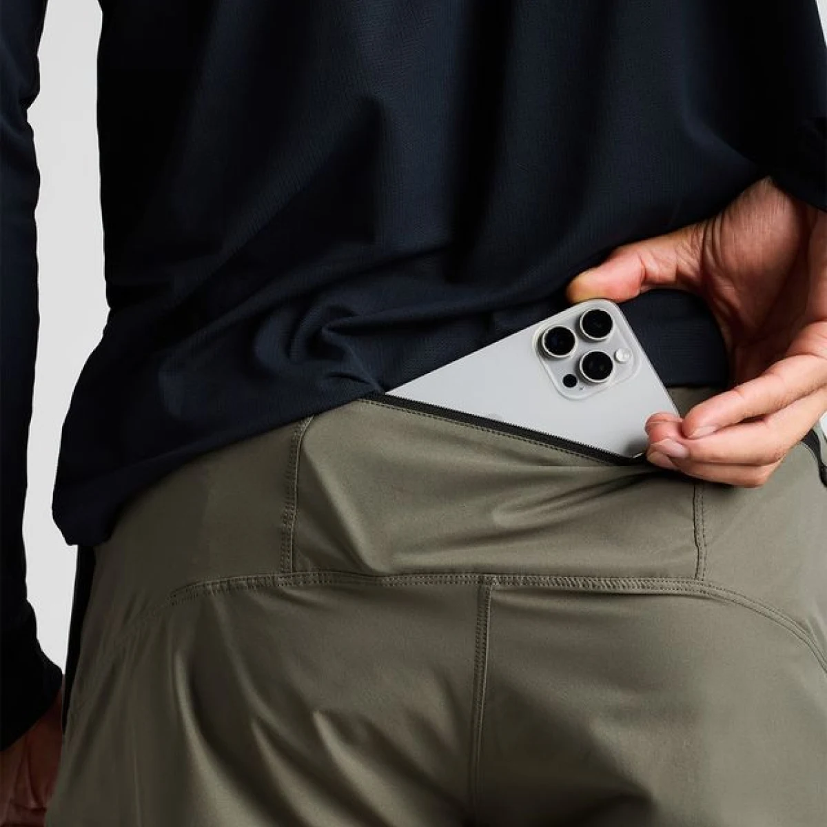 A close-up of a person putting a smartphone into the zippered back pocket of their pants.