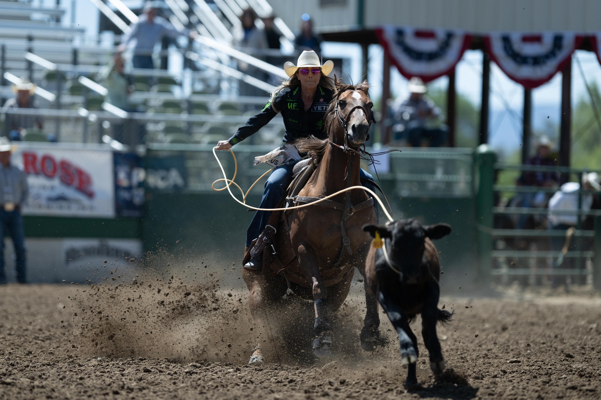 Rodeo rider on horseback chasing a calf in a dusty arena.