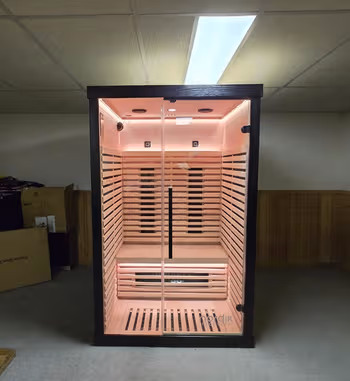 A personal indoor sauna with a dark frame, glass door, and a wooden interior lit with warm light.