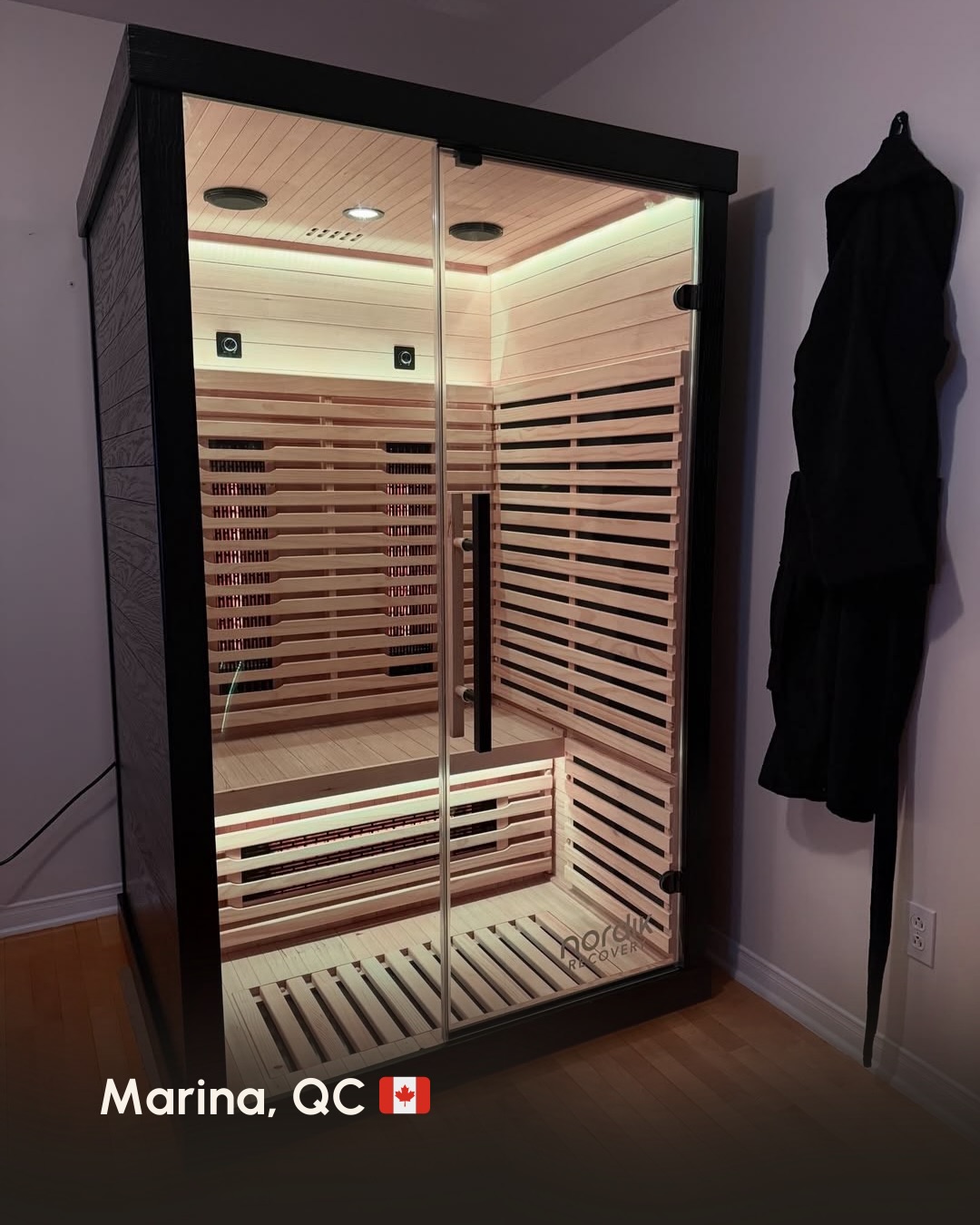 A home infrared sauna with a black frame and glass door, showing the illuminated wood interior.