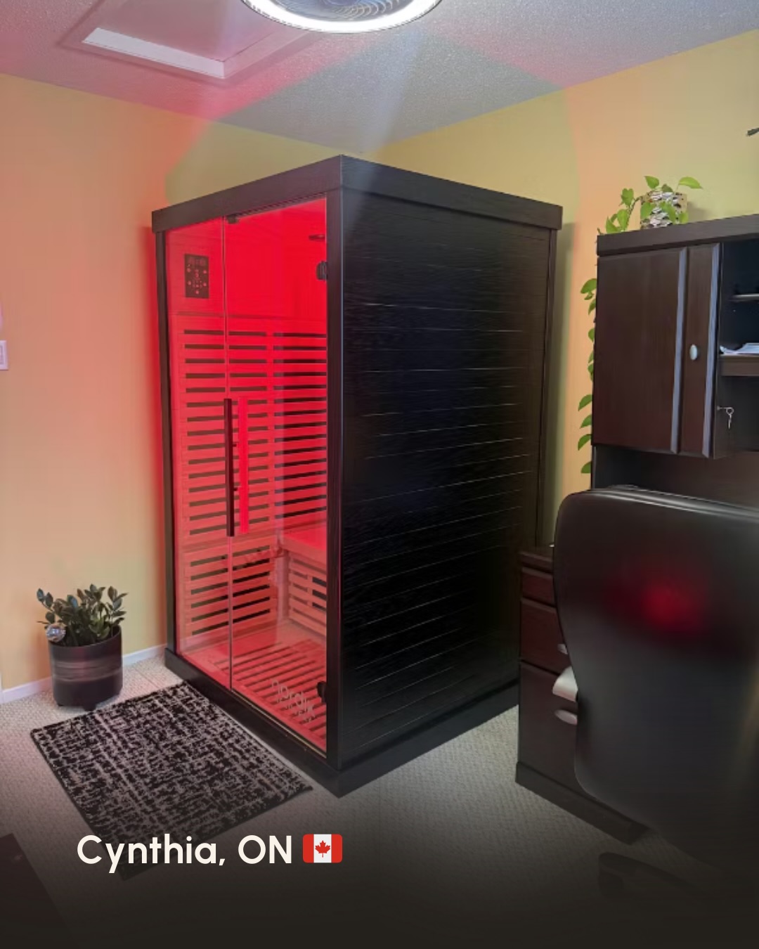 A black personal sauna with red interior lighting sits in the corner of a carpeted room.