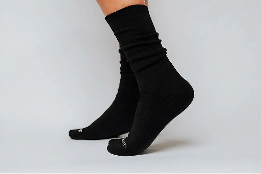 A close-up of a person's feet wearing black, slouched crew socks against a plain white background.