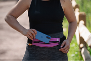 A person in athletic wear places a blue smartphone into a pink running belt.