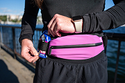 A person in athletic wear adjusts a small can in the holder of a pink running belt.