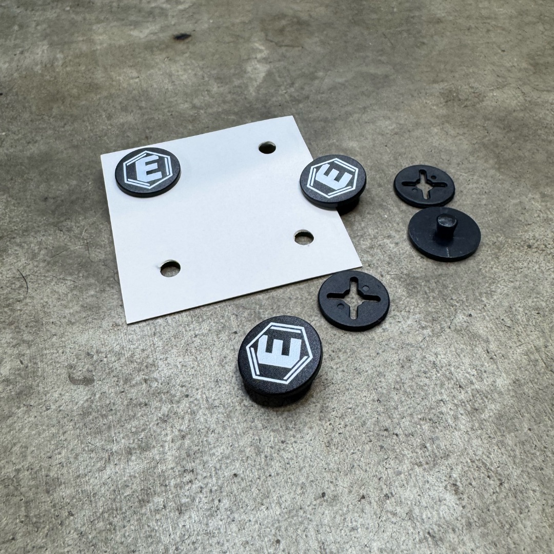 Black plastic fasteners with a white letter 'E' logo and a white plate on a concrete surface.