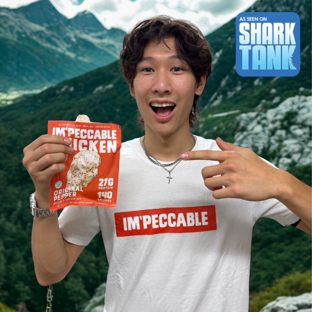 Person holding an 'IM'PECCABLE CHICKEN' package, smiling with mountains in the background.