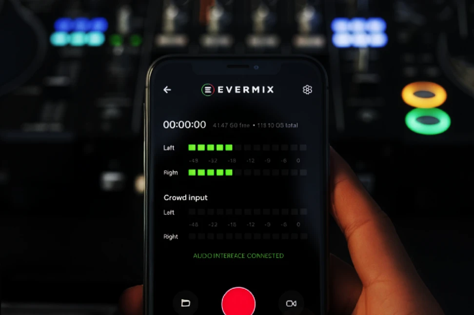 A hand holds a smartphone showing the EVERMIX app in front of a dimly lit DJ mixer.