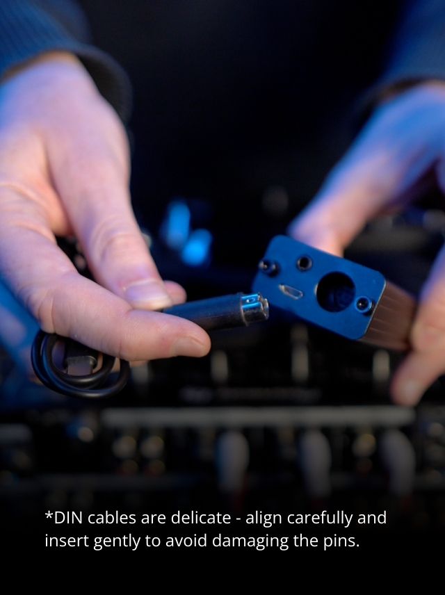 Hands holding a DIN cable and connector with a cautionary text overlay.
