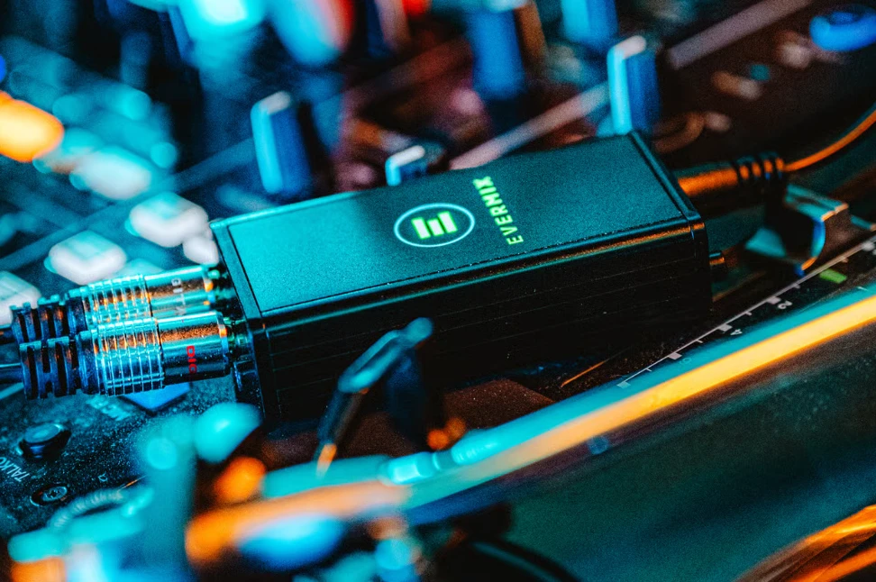 A close-up of a black Evermix audio device plugged into a sound mixing console with cables.