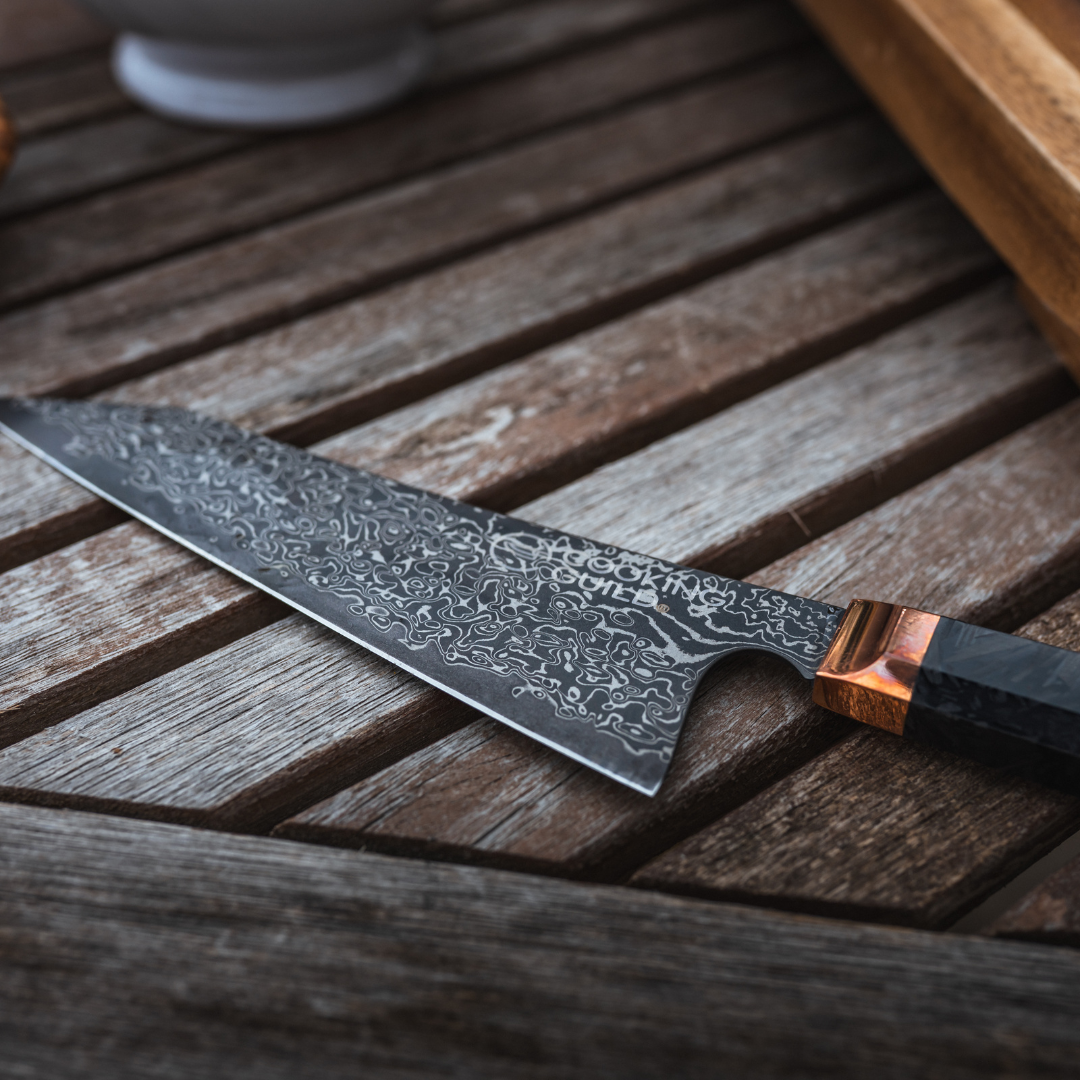 A decorative chef's knife with a patterned blade on a wooden surface.