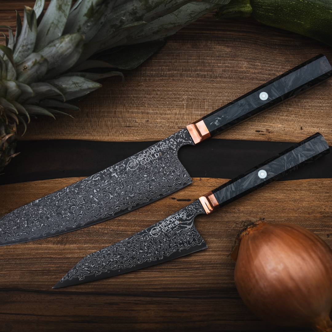 Two patterned knives on a wooden surface with pineapple and onion.