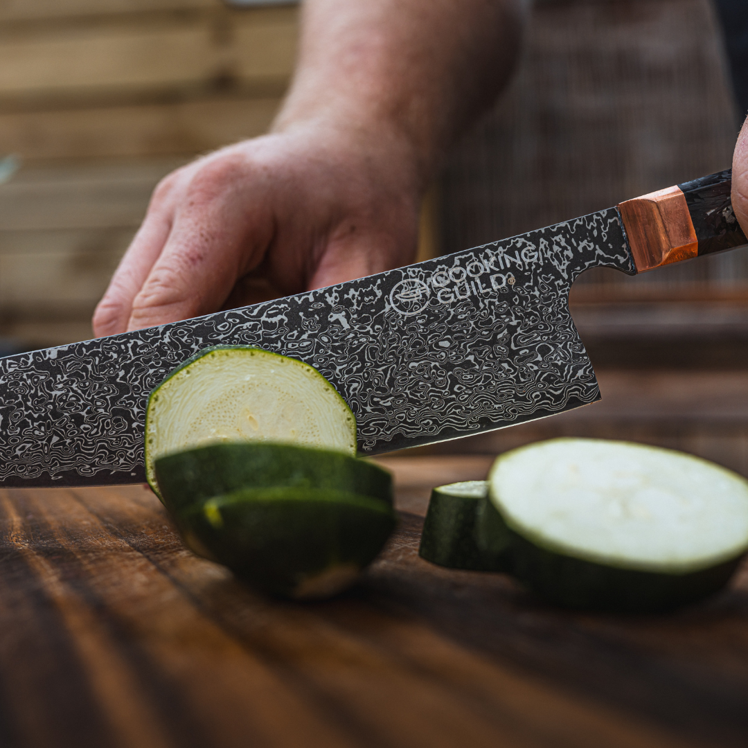 Hand slicing zucchini with a patterned knife on a wooden surface.
