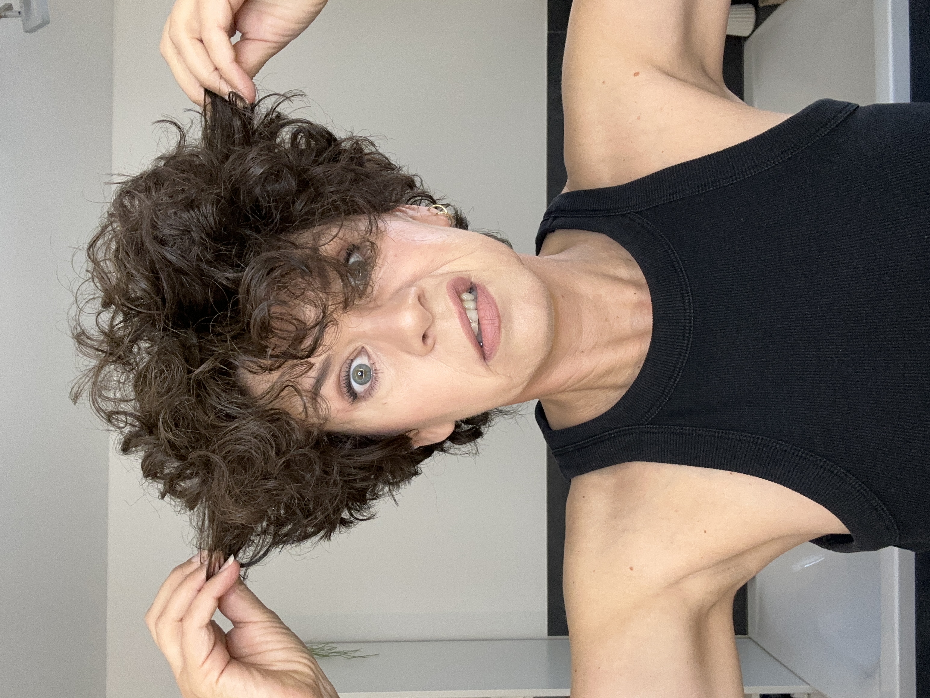 Person with curly hair making a funny face, pulling hair with both hands.
