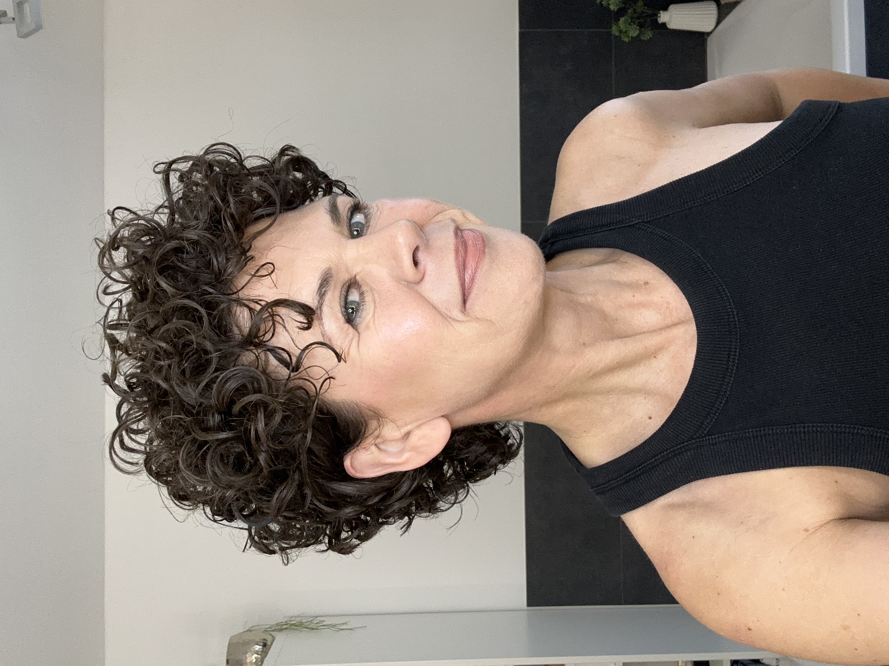 Person with curly hair wearing a black tank top, smiling slightly.