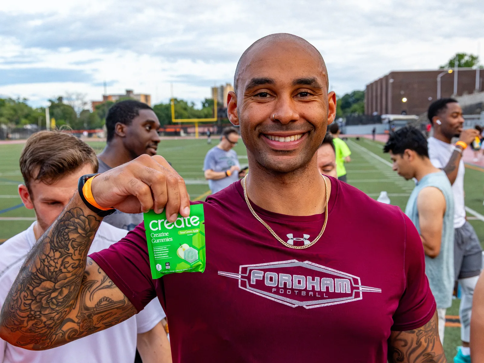 Smiling run club member holding a Sour Green Apple pack of Create gummies on the field