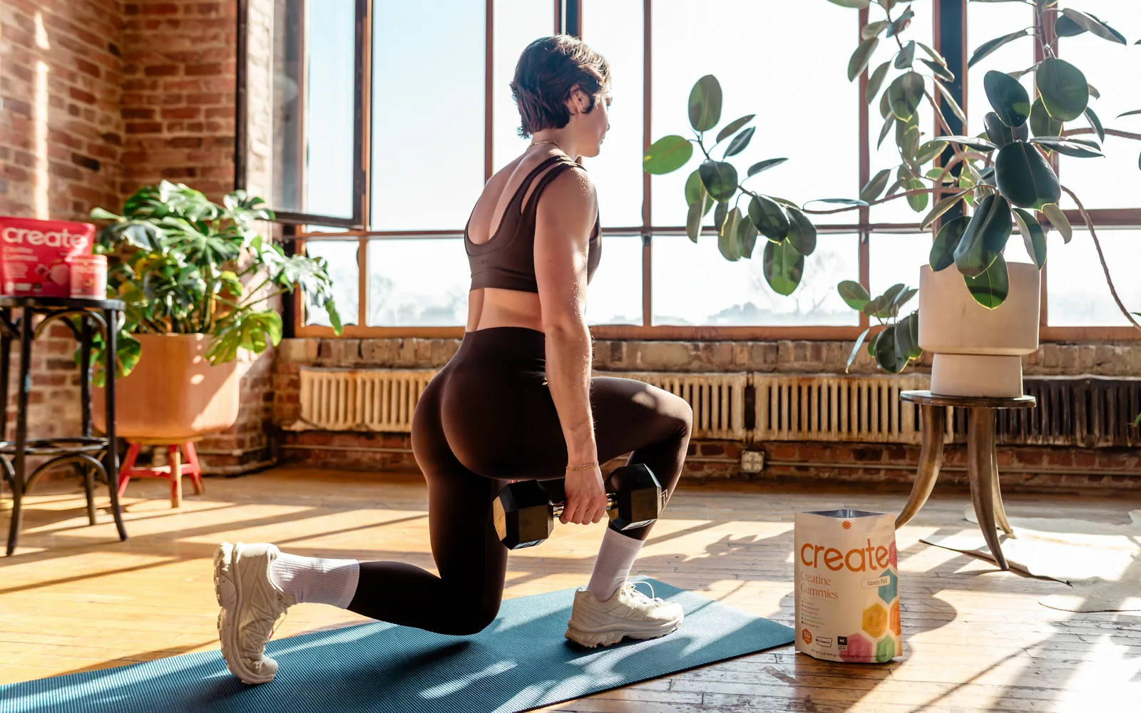 A woman doing lunges at home with a Create pouch on the floor nearby