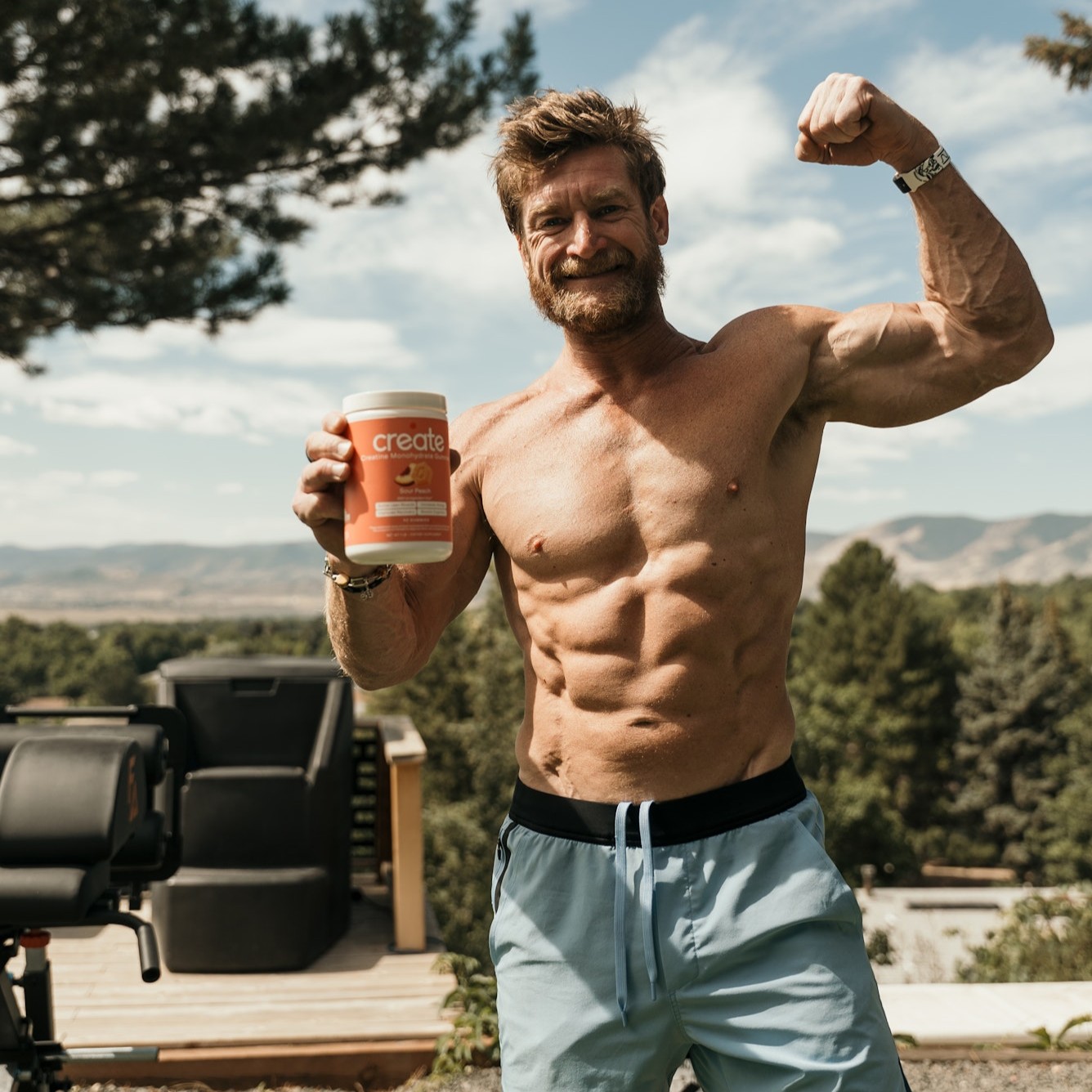 Shirtless man flexing and holding a container outdoors.