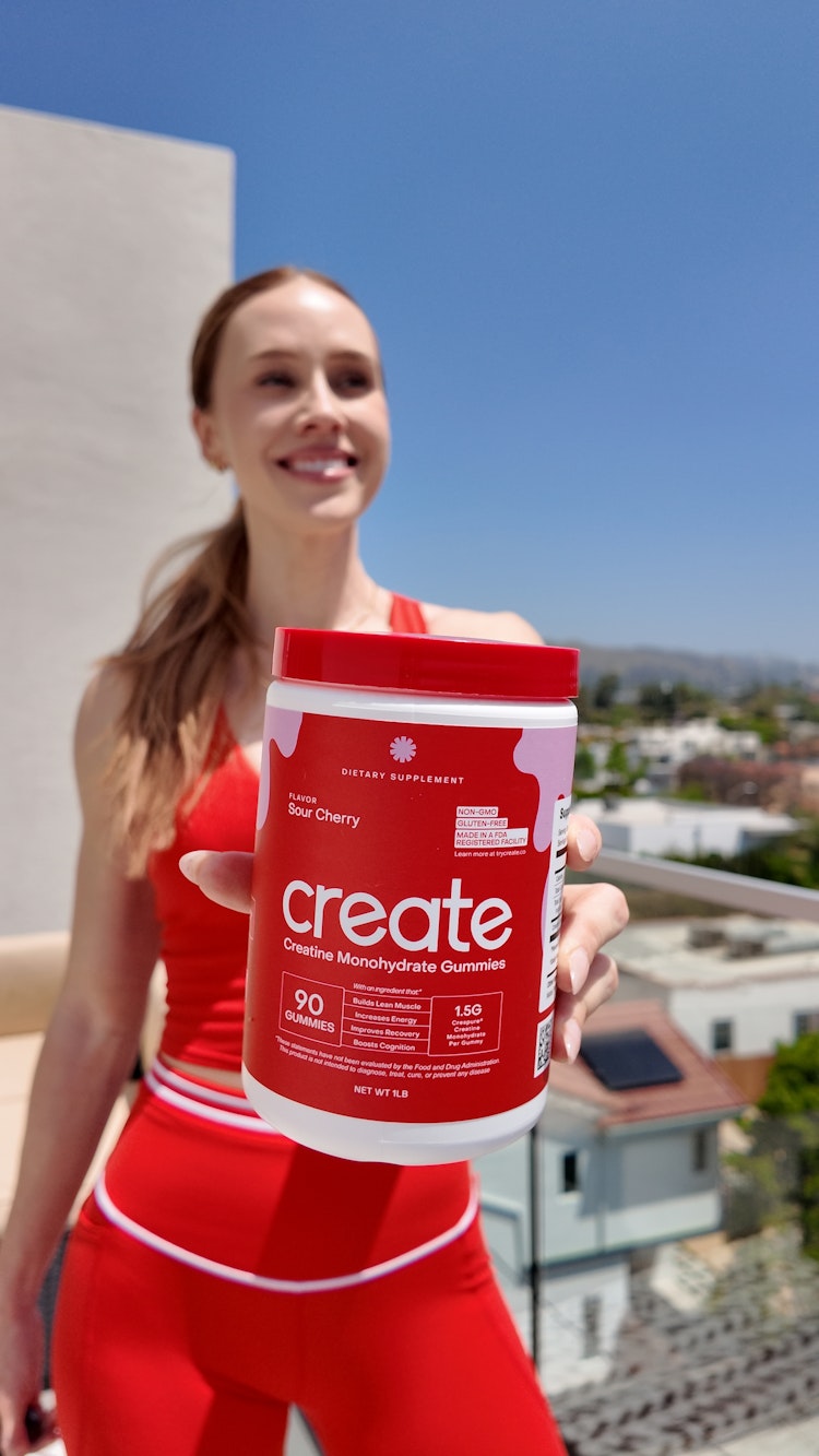 Person holding a container of creatine monohydrate gummies outdoors.