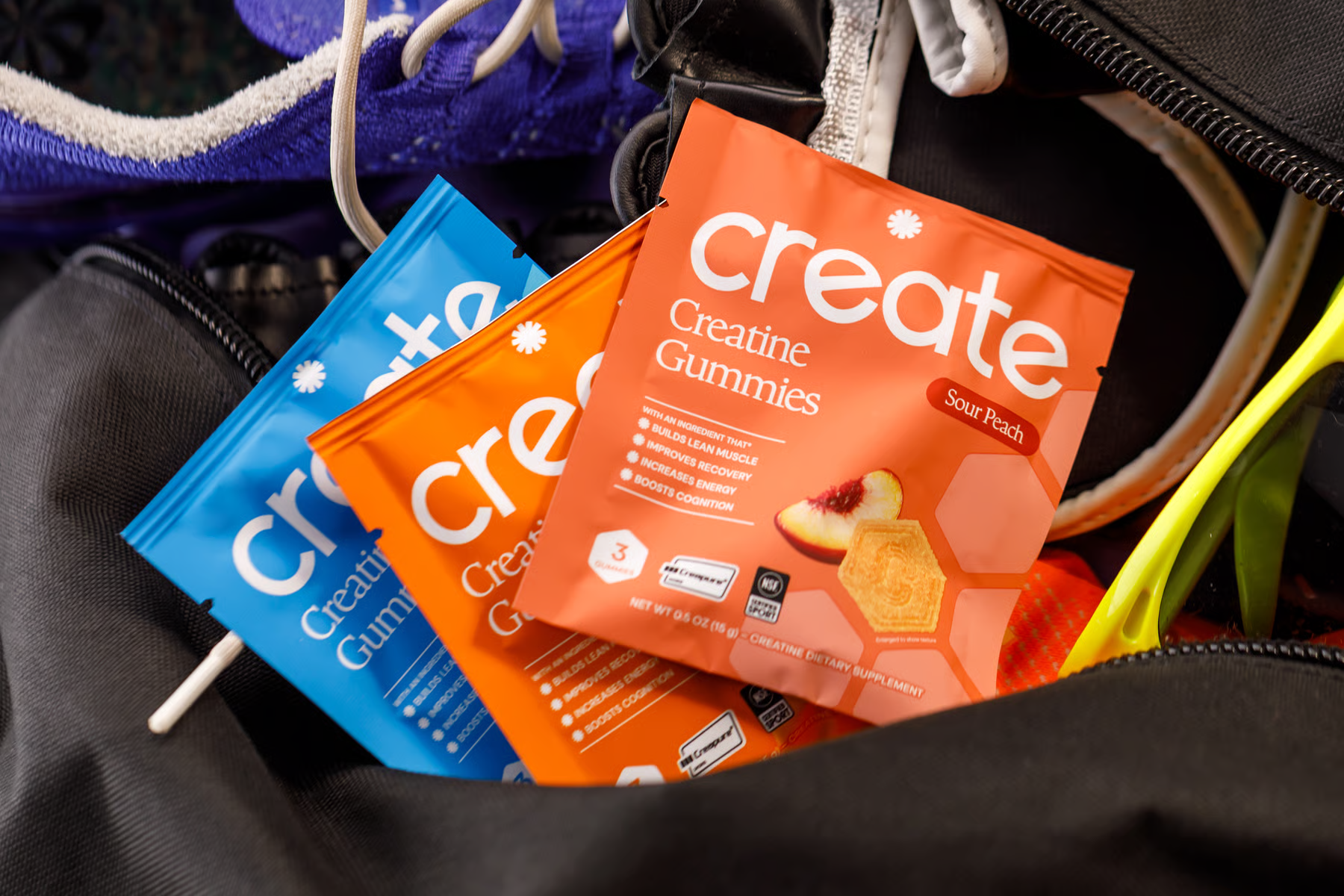 Several colorful packets of Create Creatine Gummies sticking out of an open black gym bag.