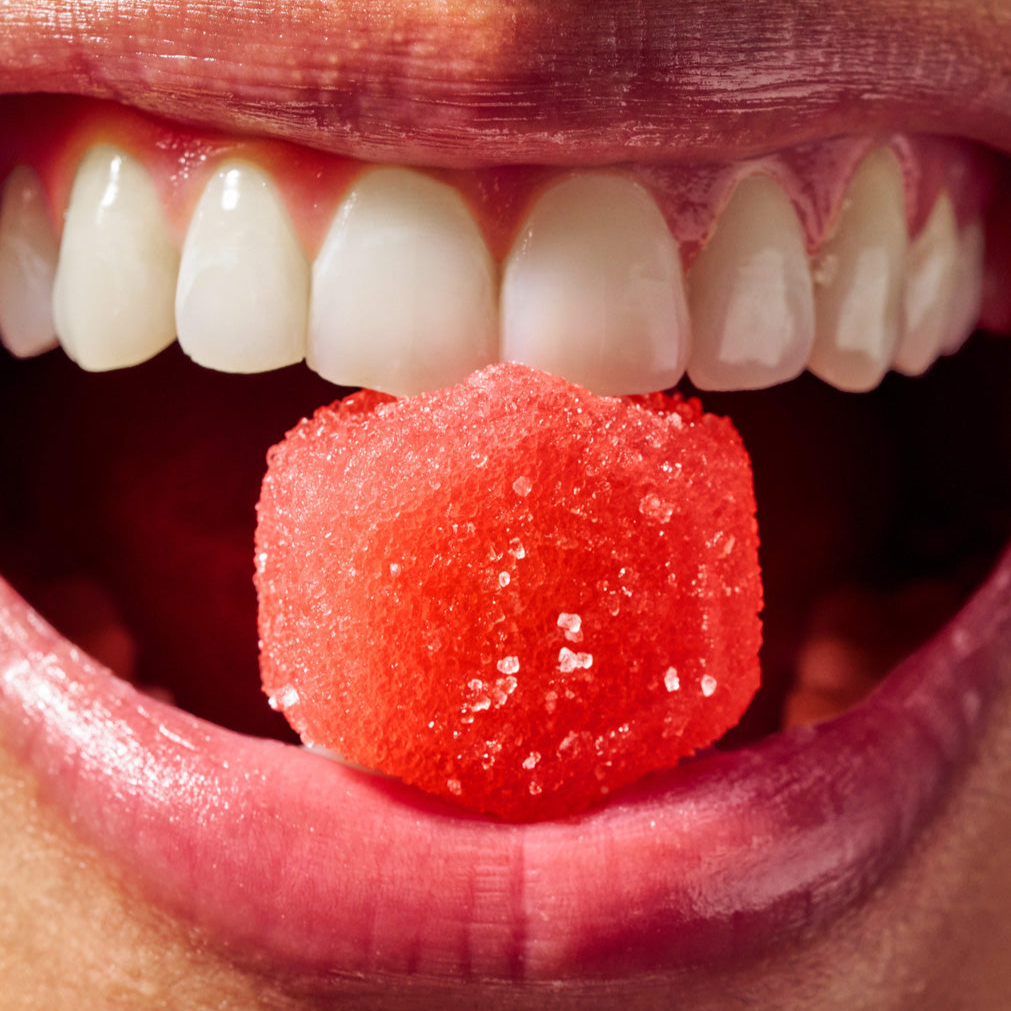 Close-up of a mouth holding a red sugar cube on the tongue.