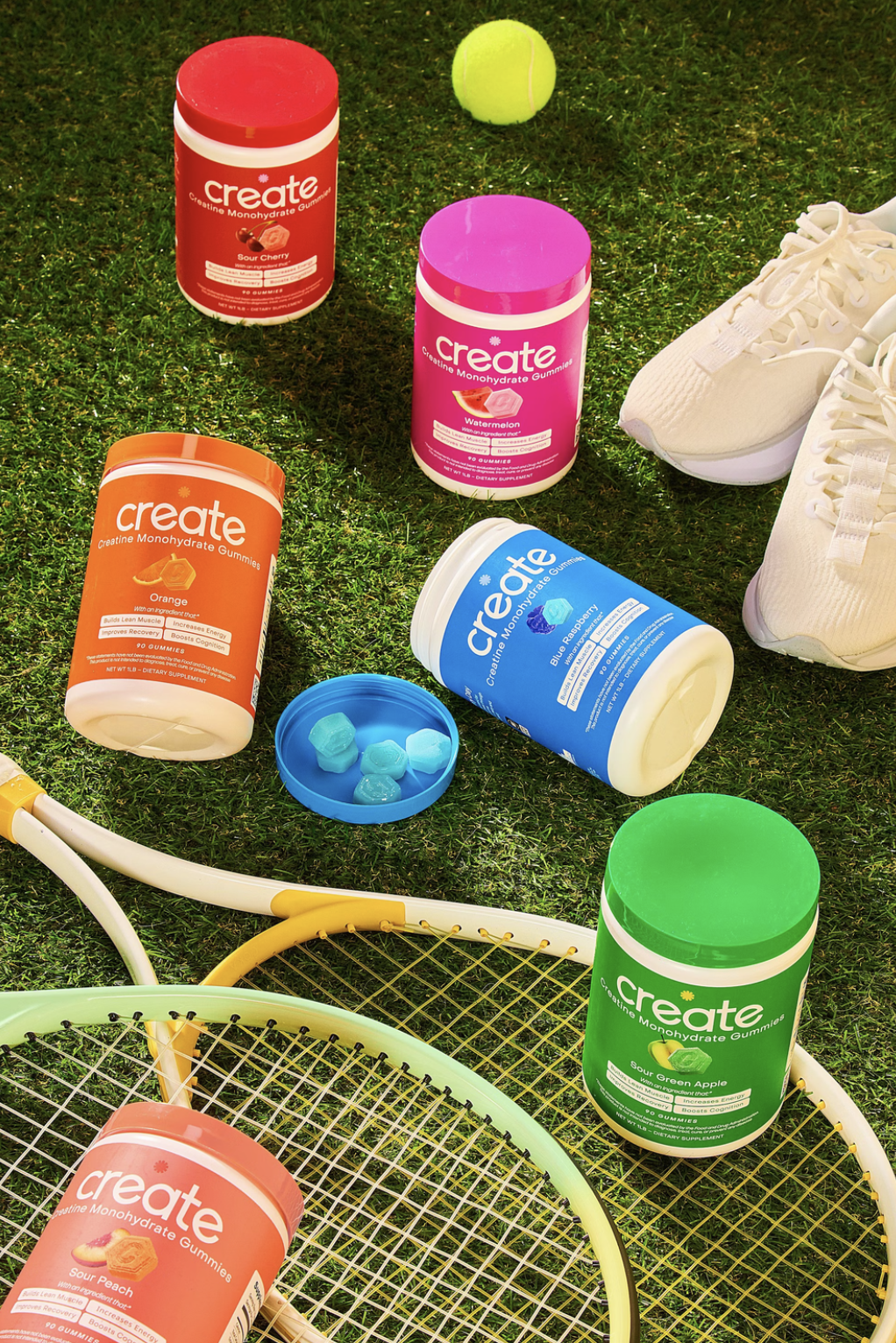 Colorful gummy containers on grass with tennis rackets and shoes.