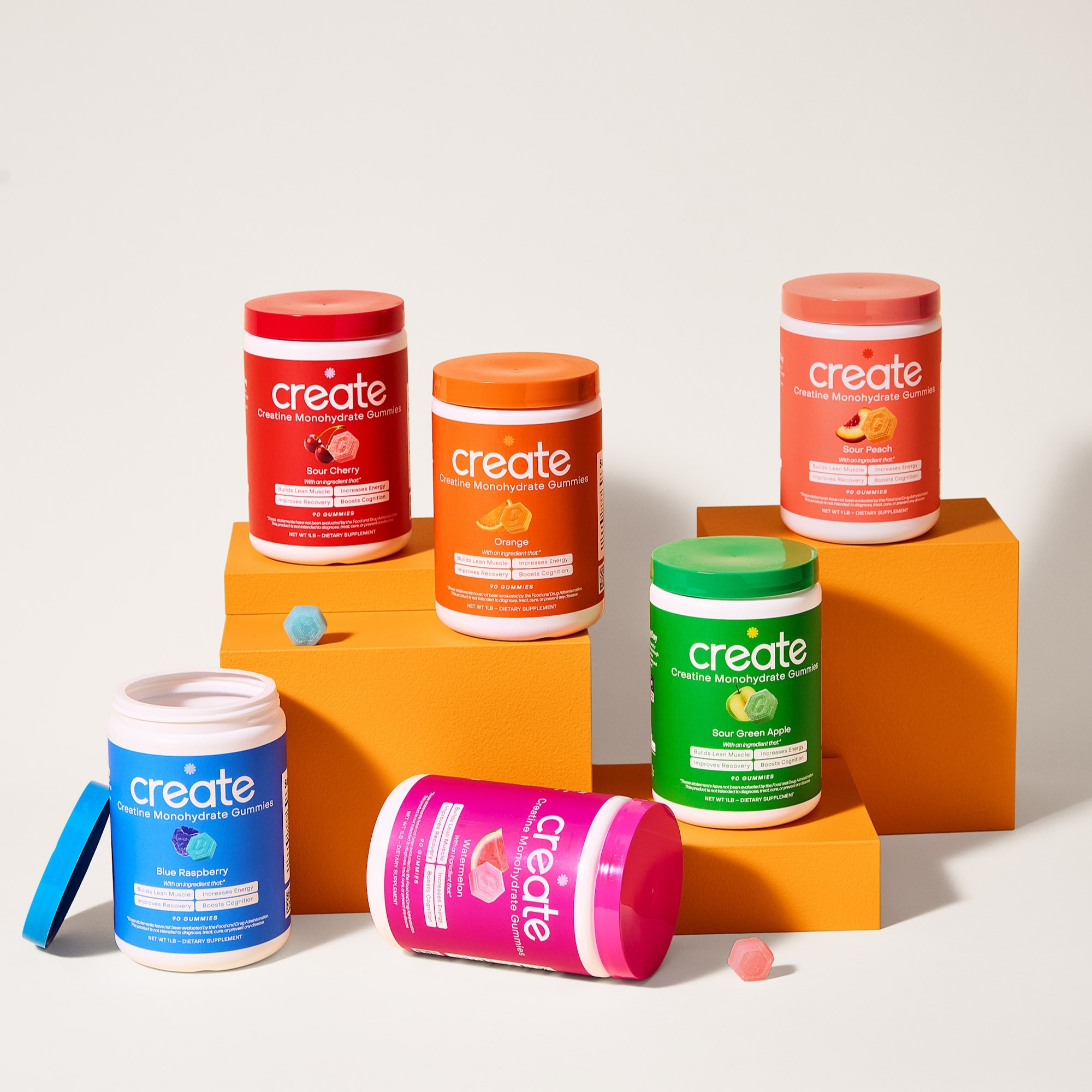 Colorful jars of creatine monohydrate gummies on orange blocks.
